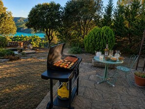 Churrasqueira ao ar livre com comida, uma mesa com bebidas e uma vista panorâmica ao fundo.