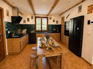 Cozinha com mesa de madeira posta para o café da manhã, uma geladeira preta e uma janela com vista.