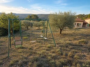 Um balanço em uma área gramada, com árvores e uma casa ao fundo.