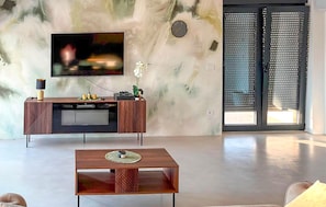 Un salon moderne avec un téléviseur à écran plat fixé au mur, une table basse en bois et une grande fenêtre offrant une belle vue.
