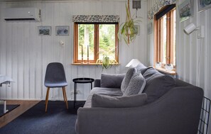 A cozy living room with a grey sofa, a small black chair, a wooden side table, and a window with a view of greenery. - Stunning home in örkelljunga with WiFi (Örkelljunga)
