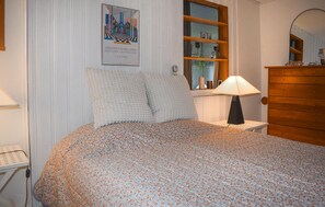 Une chambre à coucher avec un lit, une commode, une lampe, une fenêtre donnant sur un beau paysage et une affiche accrochée au mur.