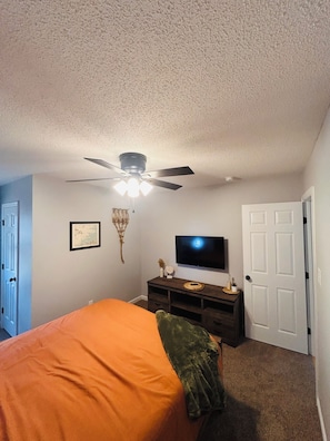 A bedroom with a bed, a ceiling fan, a television, and a door.