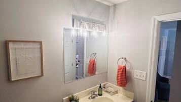 Un baño con un lavamanos blanco, gabinetes oscuros, un espejo con iluminación, un inodoro y un cuadro en la pared.