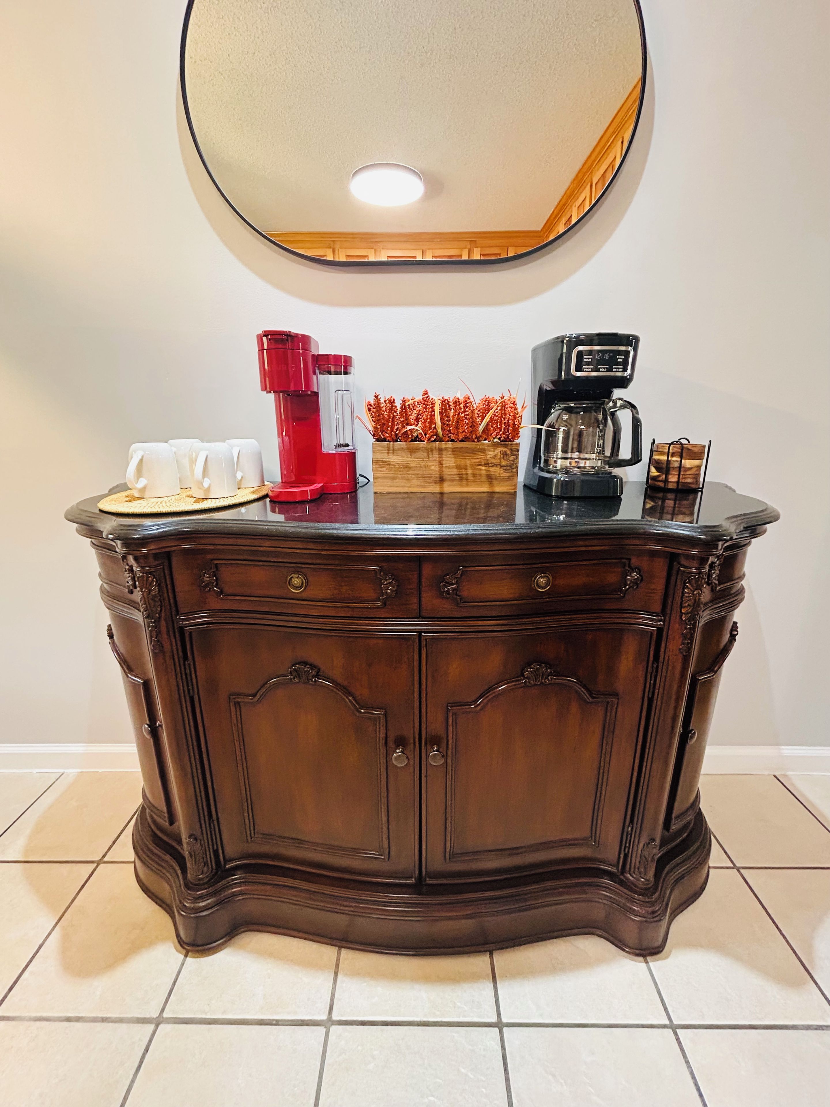 Un meuble en bois avec un miroir au-dessus, une machine à café et une petite plante posée sur le plan de travail.