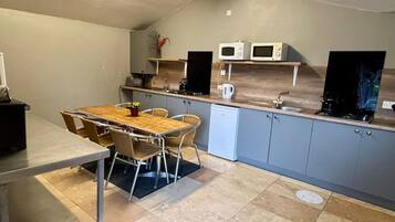 A compact kitchen with a dining table, chairs, a microwave, a kettle, and a small refrigerator.