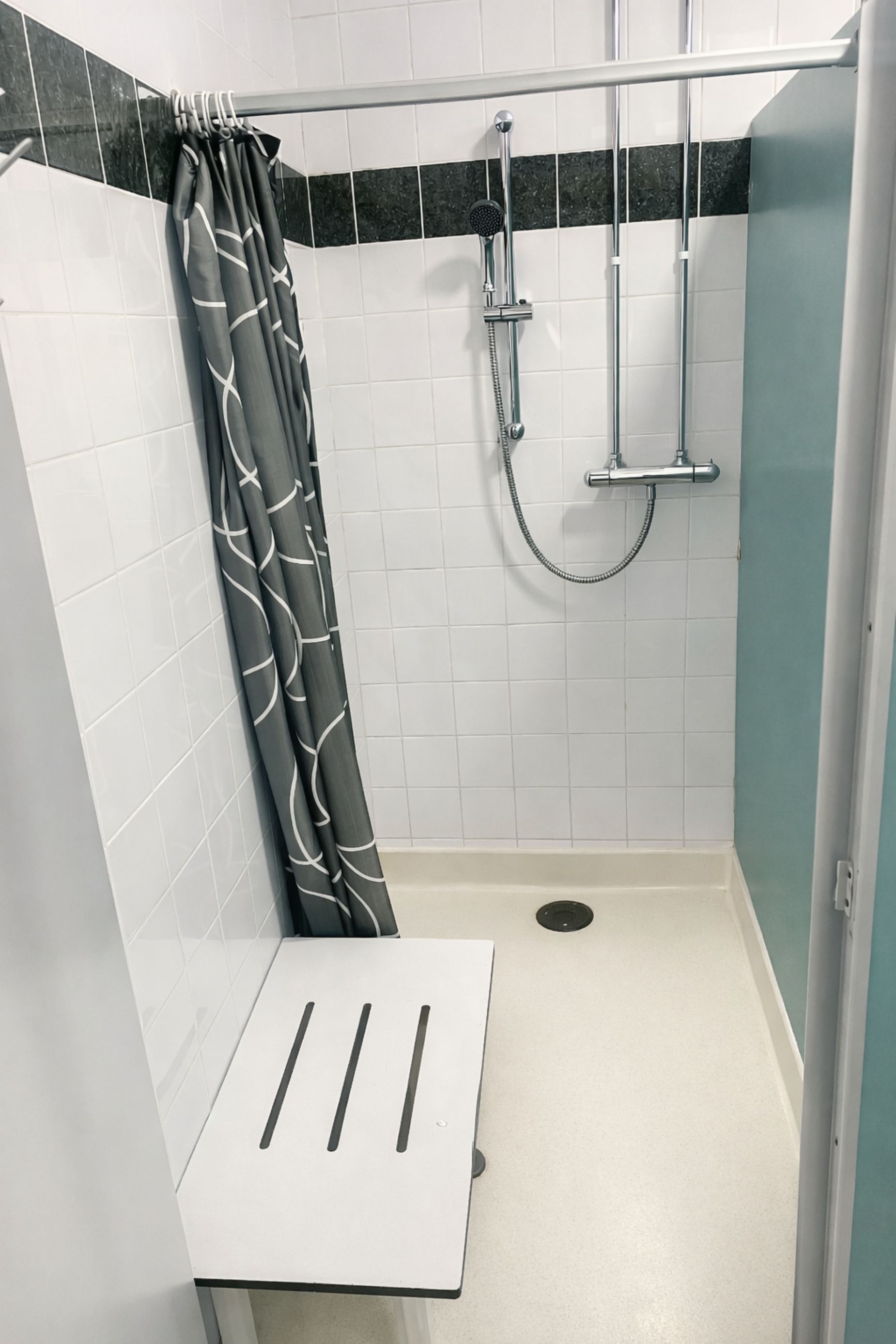 Un área de ducha con piso blanco, cortina de ducha estampada en blanco y negro, y cabezal de ducha cromado.