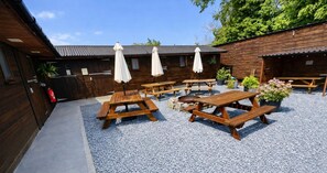 Un patio con mesas de picnic de madera y sombrillas, rodeado de edificios de madera.