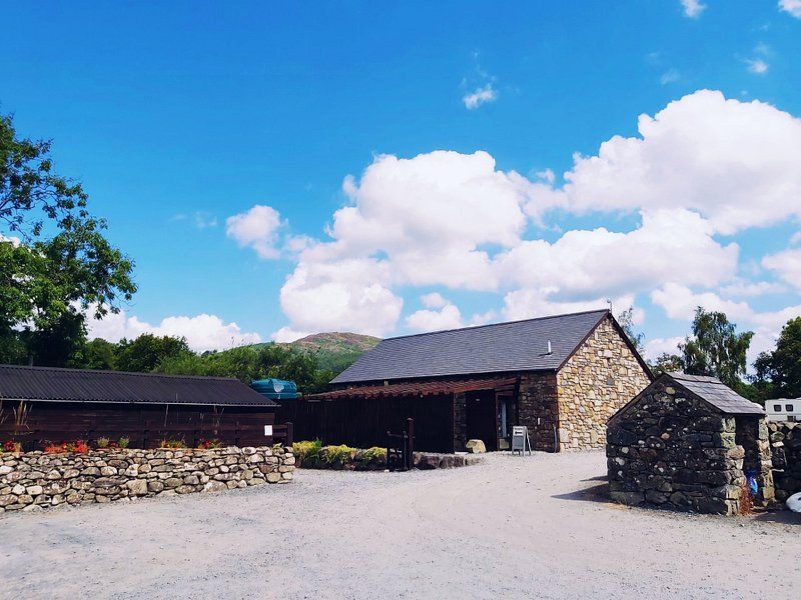 A stone building with a sloped roof, surrounded by a gravel area and a stone wall.