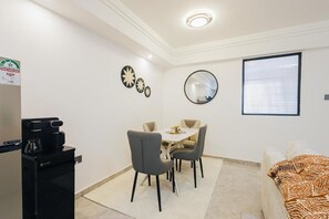 Ein kompakter Wohnbereich mit Essplatz, einer Kaffeemaschine, einem Bett und einem Fenster mit Jalousien.