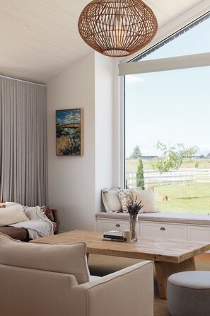 A modern living room with a large window, a woven light fixture, a painting, and a cozy seating area. - Carrick Farmhouse Luxury Retreat (Carrick)