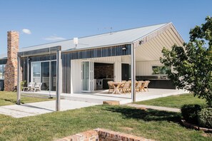 A modern house with a covered patio, a brick chimney, and a large sliding glass door leading to an outdoor kitchen. - Carrick Farmhouse Luxury Retreat (Carrick)