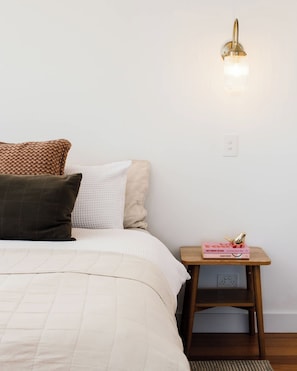 Ein Schlafzimmer mit einem Bett, Kissen, einem Nachttisch mit Lampe und einem Buch.