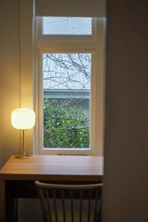 A room with a desk, chair, and a window with a view of a tree and a building. - Carinya Luxe Cottage (Newstead)