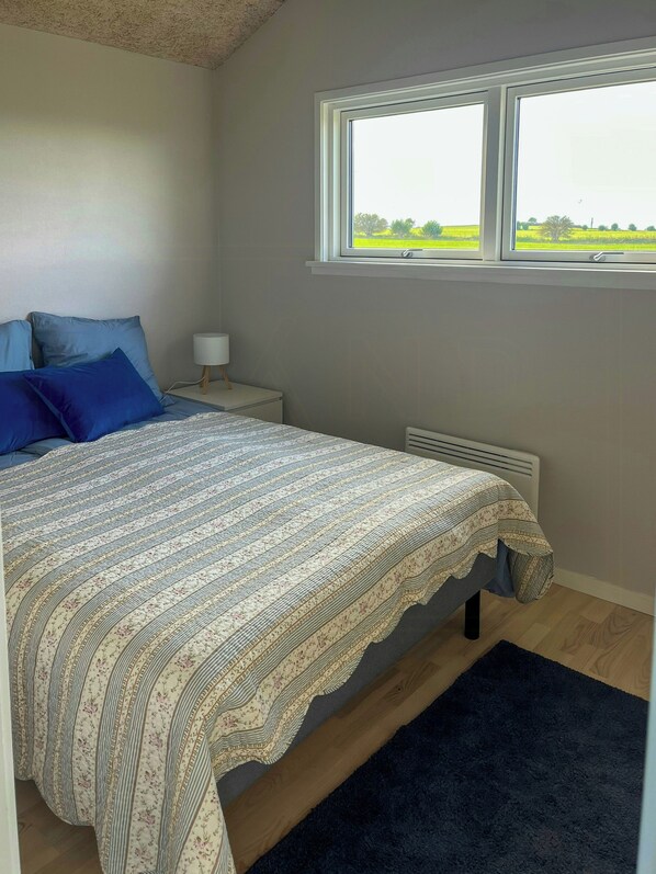 A bedroom with a bed, a nightstand, a window, and a radiator. - Holiday cottage with wild bath by field and water (Kerteminde)