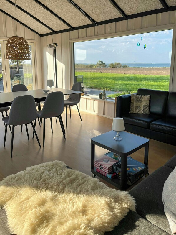 Una sala de estar moderna con un ventanal grande, un sofá, una mesa de comedor con sillas y una pequeña mesa de centro.