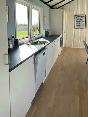 A kitchen with a window, sink, and white cabinets. - Holiday cottage with wild bath by field and water (Kerteminde)