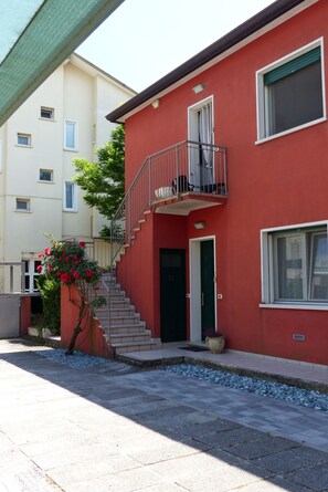 A two-story building with a red facade, a green door, and a small balcony. - Beautiful Apartment in Jesolo, PVT Parking (Jesolo)