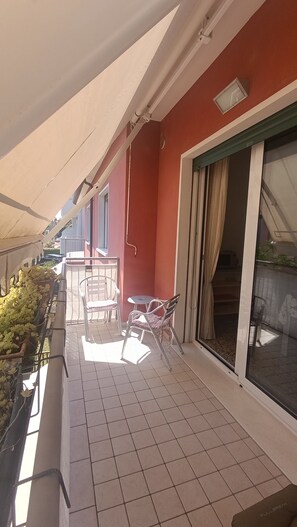 Ein Balkon mit gefliestem Boden, einem Tisch mit Stühlen, einer Topfpflanze und einer Schiebetür aus Glas.