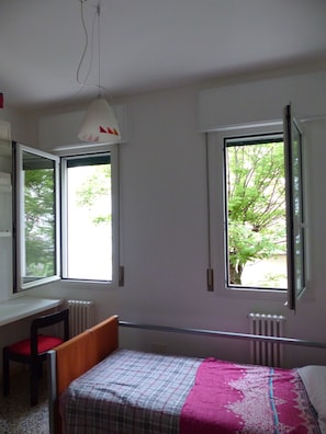 Ein Schlafzimmer mit einem Bett, einem Schreibtisch und zwei Fenstern.