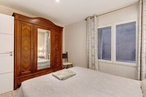 Ein Schlafzimmer mit einem Holzschrank, einem Bett mit gemustertem Überwurf, einem Stuhl und einem Fenster mit Vorhängen.