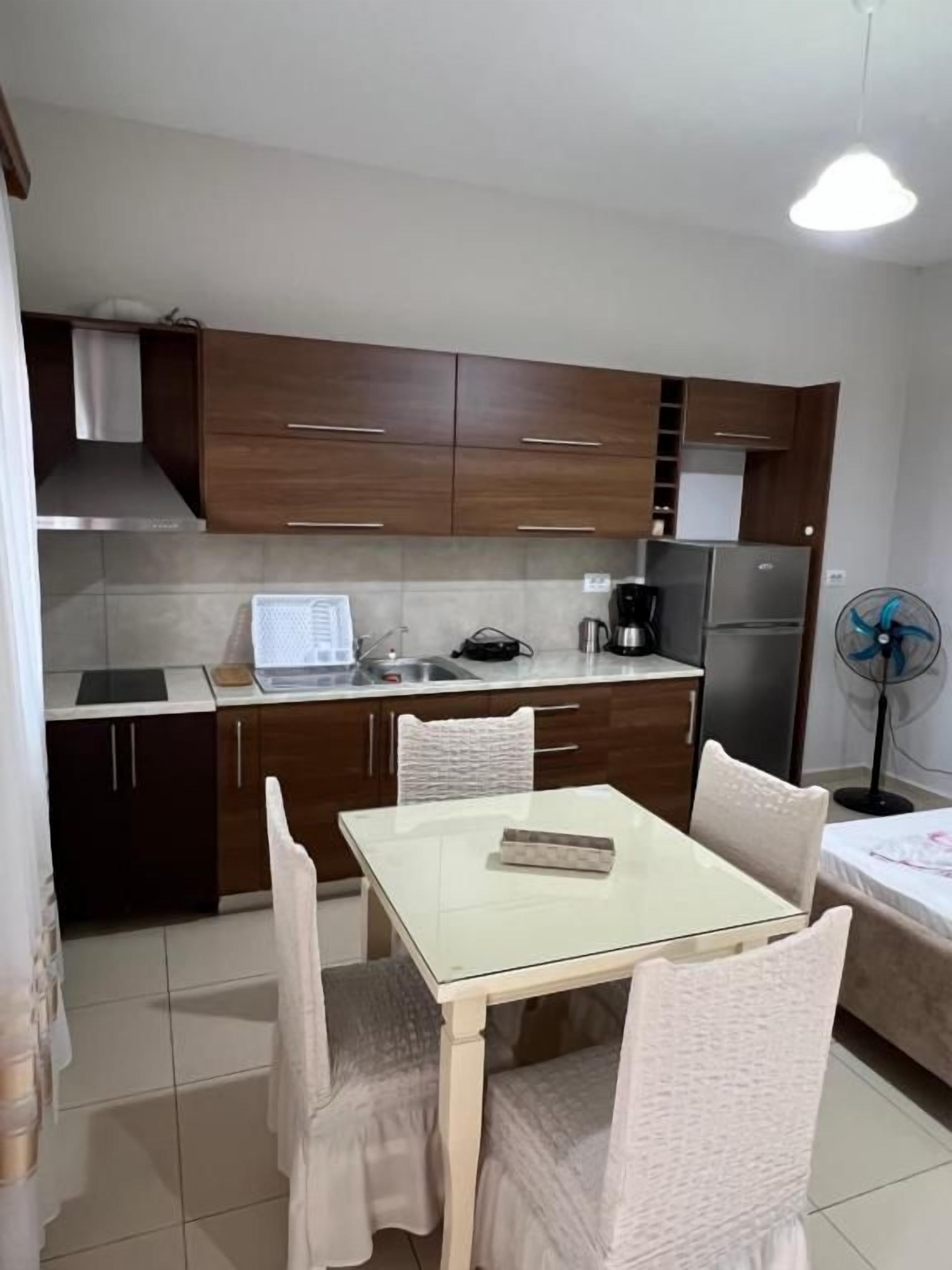 Cocina compacta con una mesa y sillas, un refrigerador, una cafetera y un ventilador.