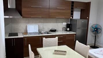 Cocina compacta con una mesa y sillas, un refrigerador, una cafetera y un ventilador.