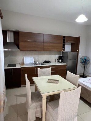 Cocina compacta con una mesa y sillas, un refrigerador, una cafetera y un ventilador.