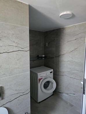 A compact laundry room with a washing machine, a dryer, and a small shelf.