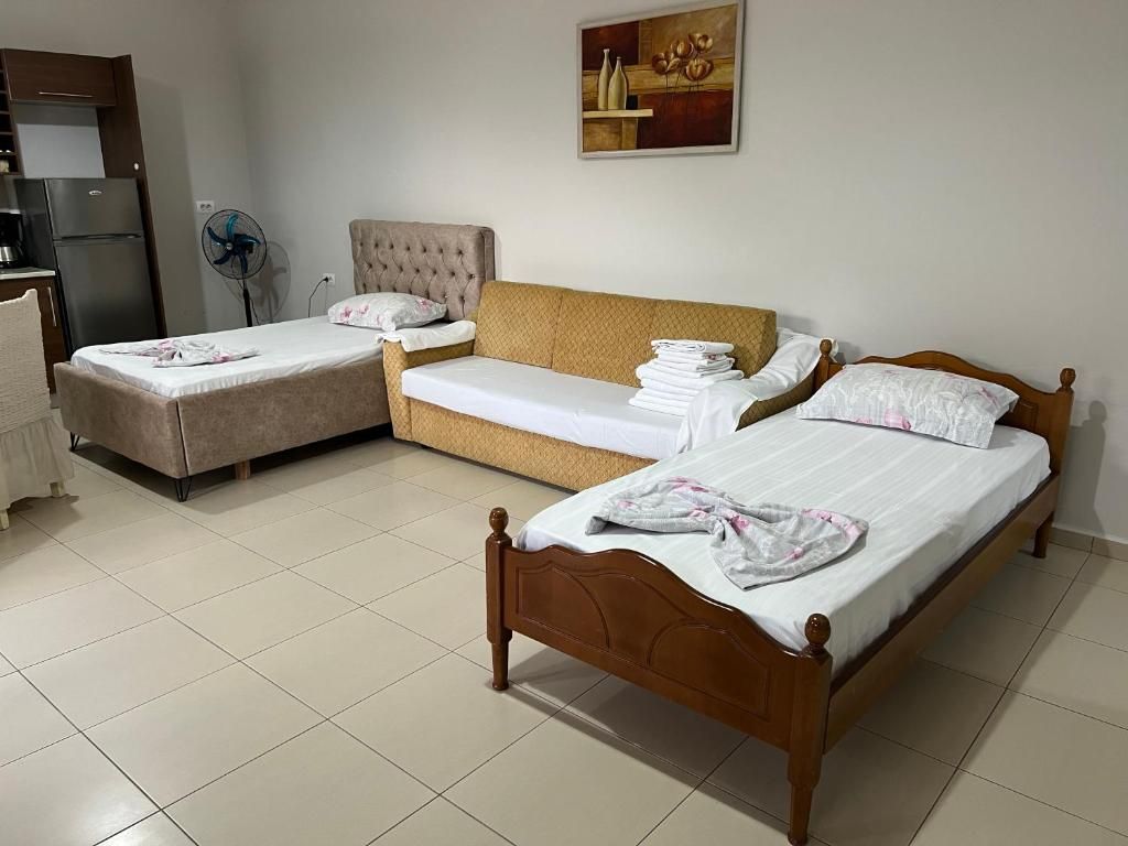 A hotel room with two beds, a sofa, a fan, and a refrigerator.