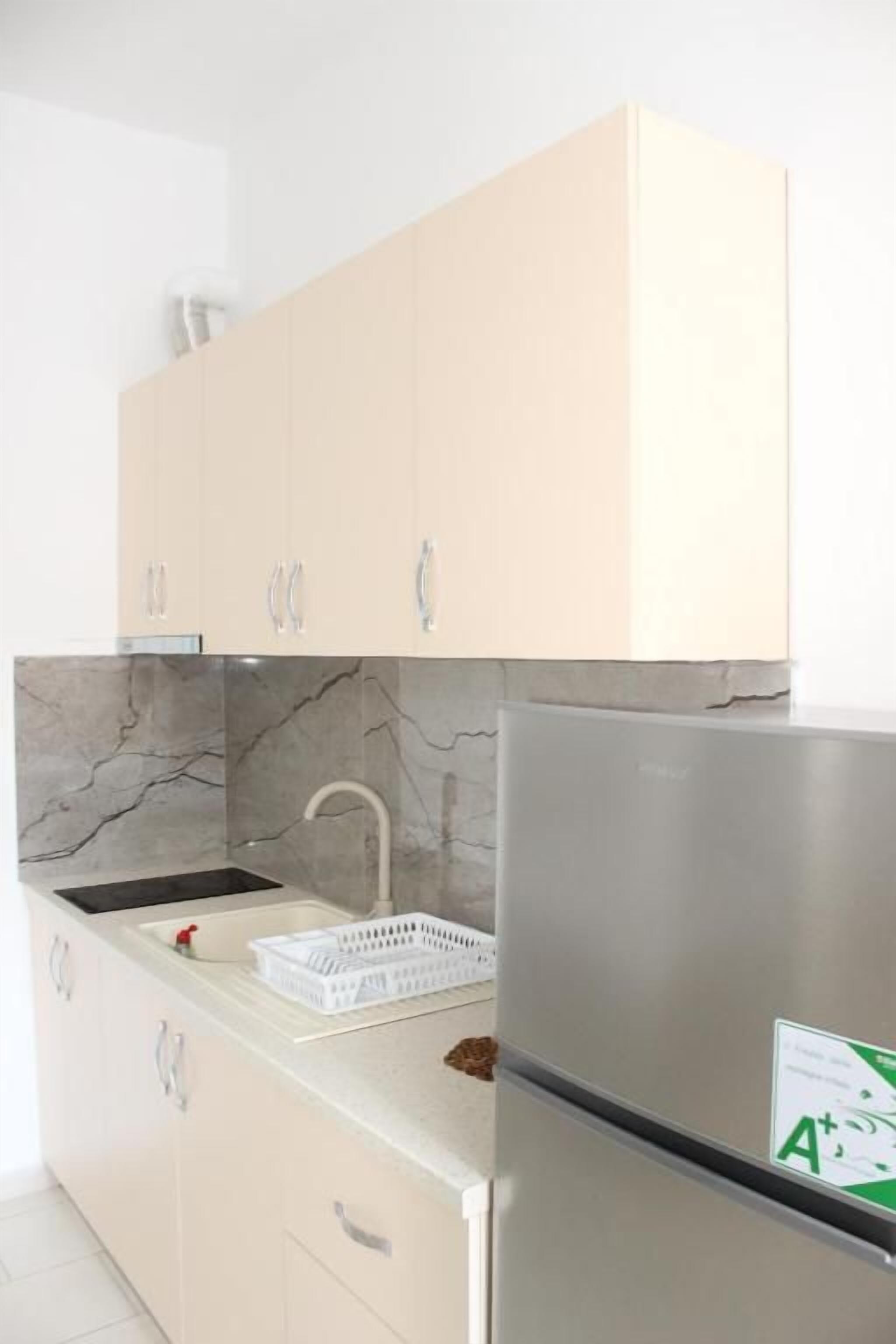 Una cocina con armarios de tonos claros, un refrigerador de acero inoxidable, un protector contra salpicaduras de mármol y una encimera blanca.