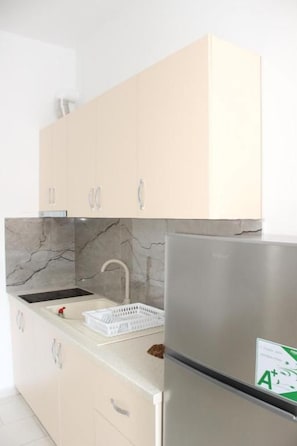 Una cocina con armarios de tonos claros, un refrigerador de acero inoxidable, un protector contra salpicaduras de m ármol y una encimera blanca.