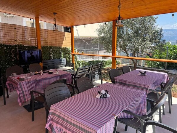 An outdoor patio with tables covered in checkered tablecloths, chairs, and a television screen.