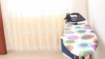 A room with a window covered by sheer curtains, a table with a colorful tablecloth, and a wall-mounted light switch.