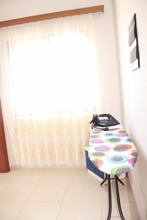 A room with a window covered by sheer curtains, a table with a colorful tablecloth, and a wall-mounted light switch.