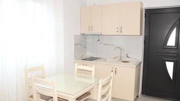 Una cocina compacta con una encimera, un lavamanos y armarios. Hay una mesa de comedor con sillas.