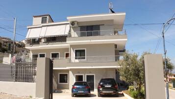 Un edificio residencial de dos pisos con un balcón en el nivel superior, entrada protegida por un portón y dos coches estacionados.