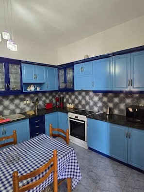 Una cocina con armarios azules, mantel a cuadros y horno blanco.