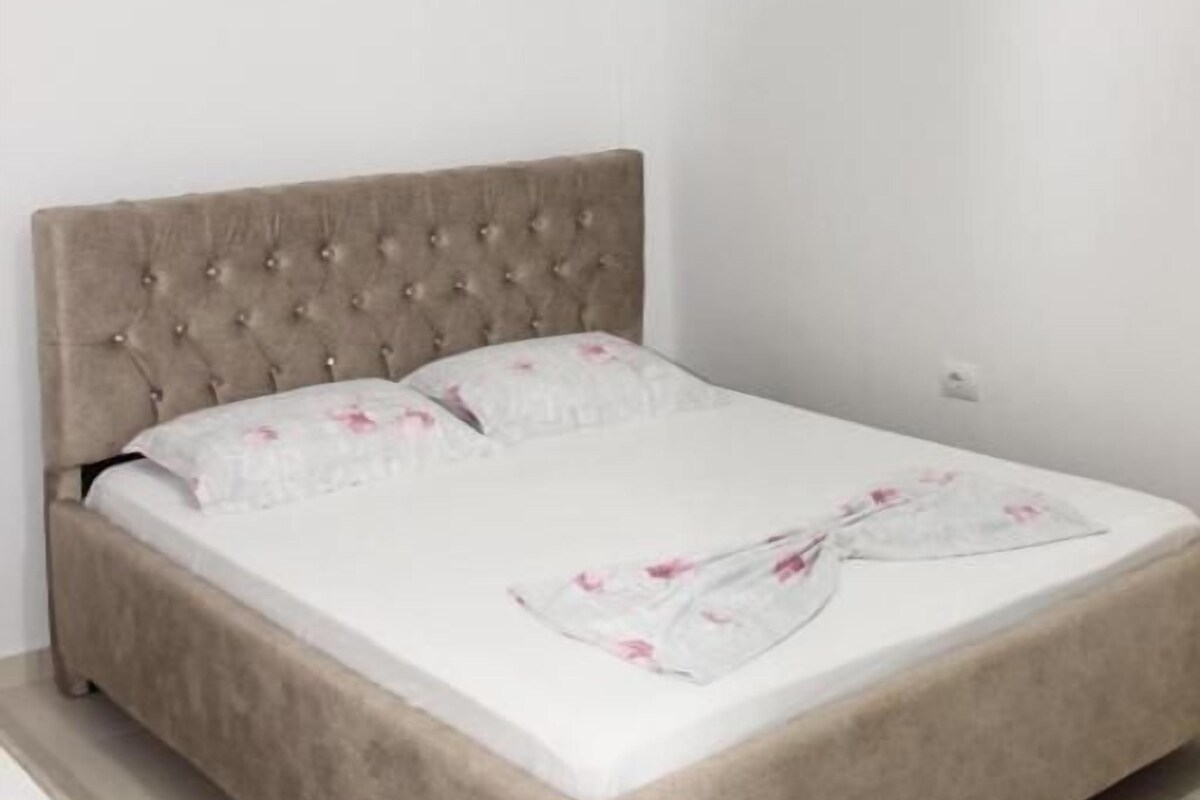 Una cama con cabecera capitonada, colchón blanco y colcha de estampado floral.