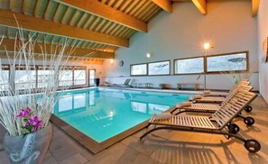 Ein Hallenbad mit Liegestühlen, Holzbalken und großen Fenstern.