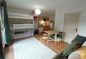 Ein kleines Zimmer mit Etagenbetten, einer Küchenzeile, einem Essbereich mit Hocker und einer Tür.
