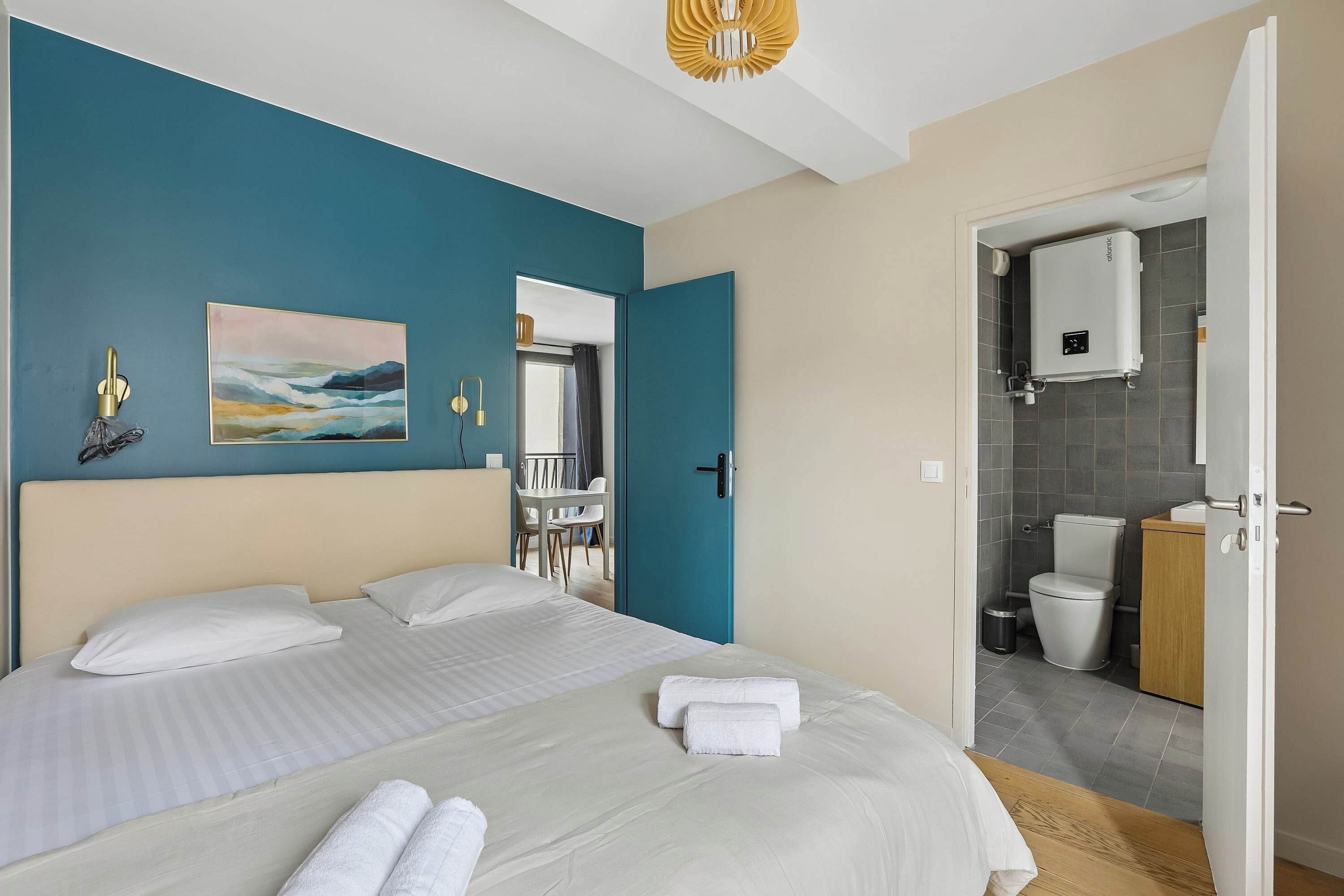A hotel room with a bed, a painting, a bathroom with a toilet, and a shower area.