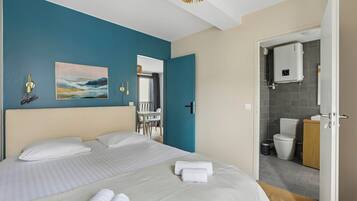 A hotel room with a bed, a painting, a bathroom with a toilet, and a shower area.