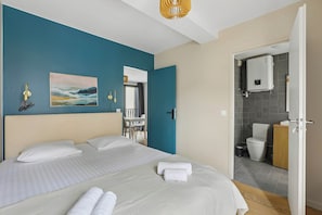 A hotel room with a bed, a painting, a bathroom with a toilet, and a shower area. - Charming Apartment with Cozy Open-Plan Living (Boulogne-Billancourt)