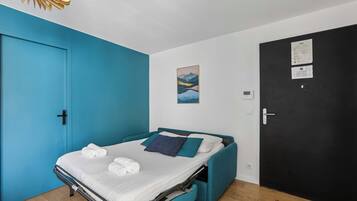 A compact bedroom with a bed, a blue wall, a black door, and a small painting.