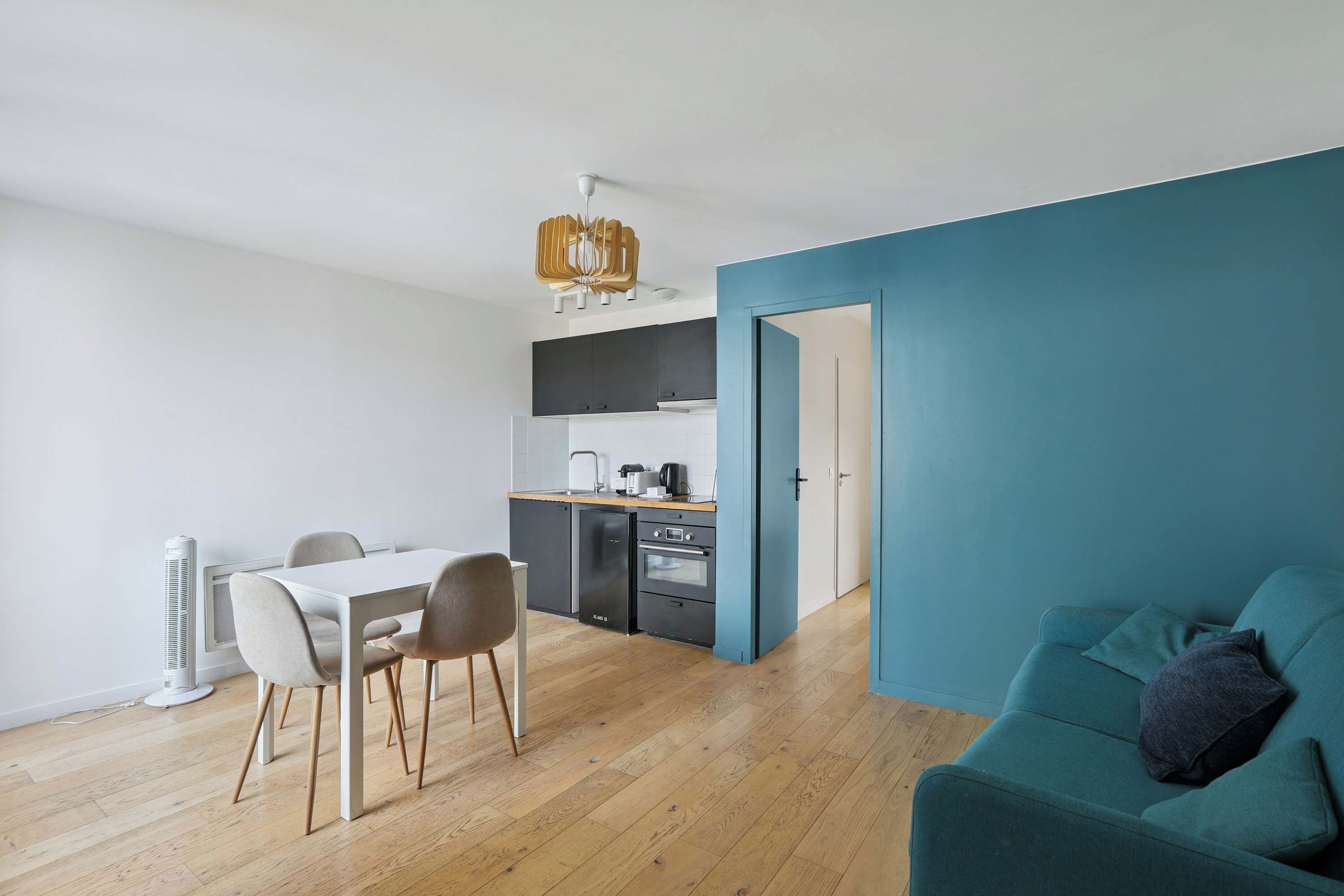 A modern apartment with a dining area, kitchenette, and a teal-colored living space.