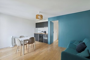 A modern apartment with a dining area, kitchenette, and a teal-colored living space. - Charming Apartment with Cozy Open-Plan Living (Boulogne-Billancourt)