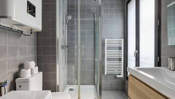 A modern bathroom with a glass-enclosed shower, a white toilet, a sink, and a towel rack.