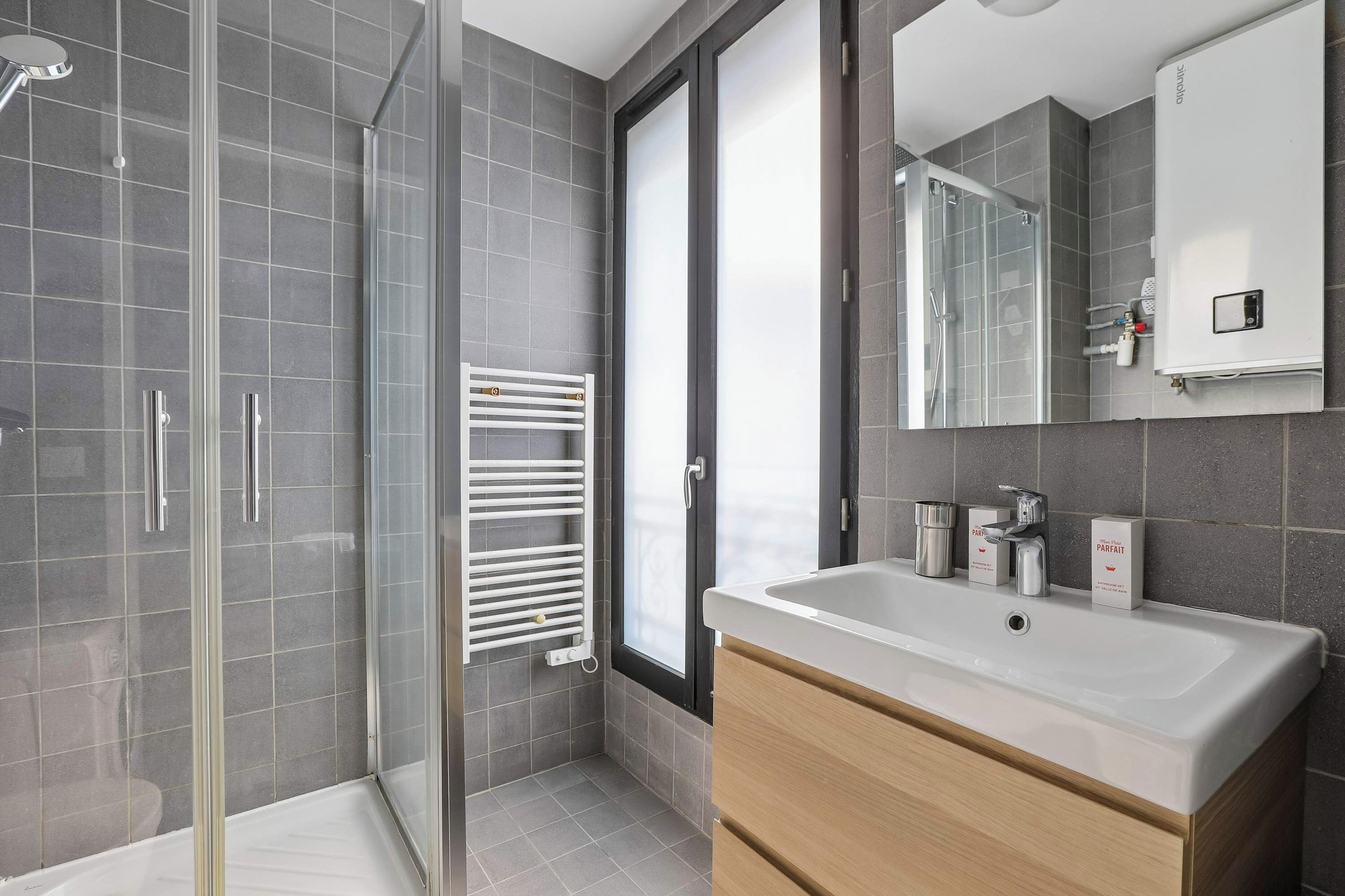 A modern bathroom with a glass shower enclosure, a white sink, and a large mirror.
