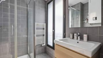 A modern bathroom with a glass shower enclosure, a white sink, and a large mirror.